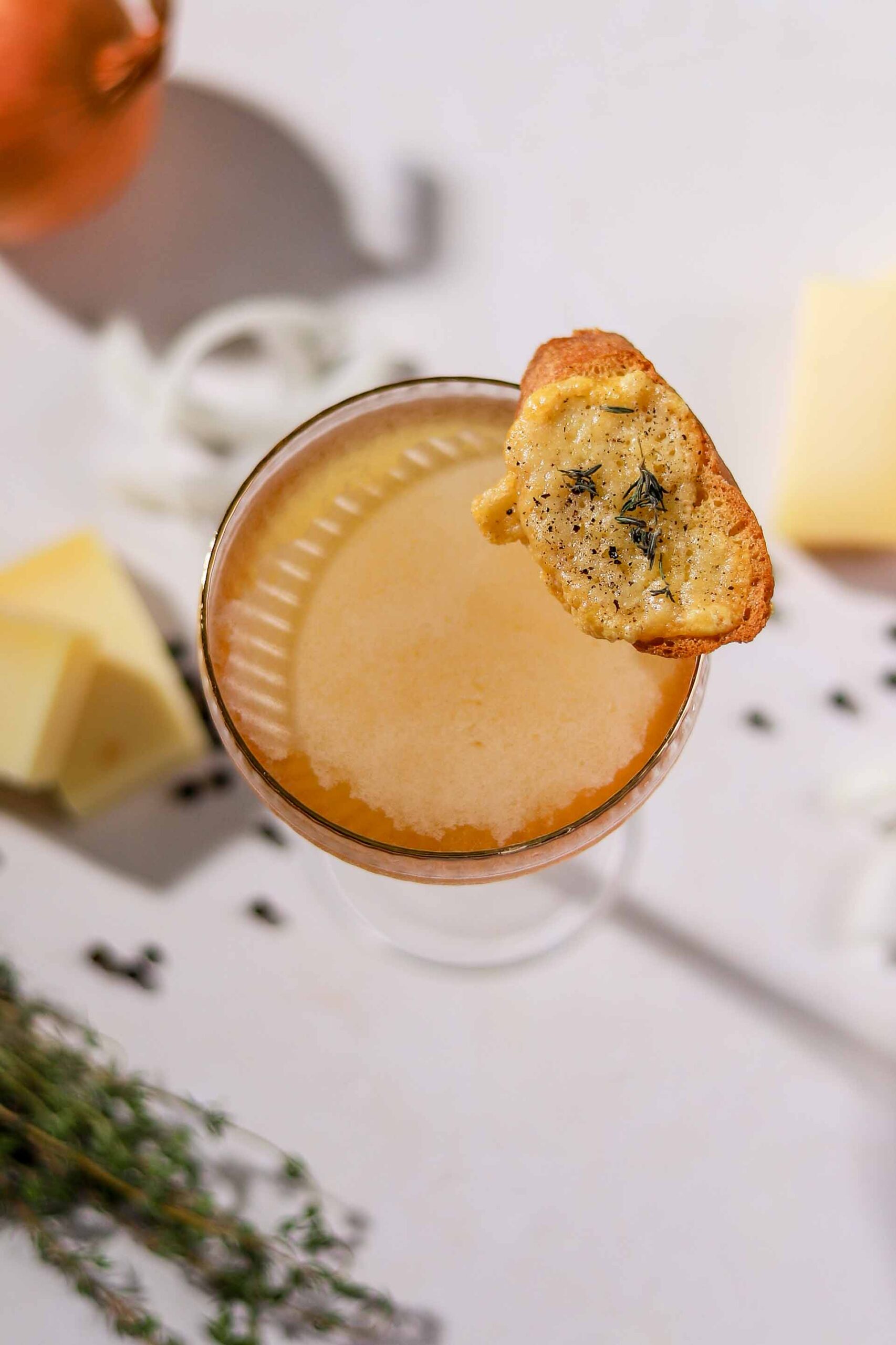 Close-up of a French onion soup martini in a ribbed coupe with a thyme and Gruyère toast garnish