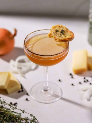 French onion soup martini in a coupe glass garnished with a Gruyère toast, with onions, thyme and cheese on the side