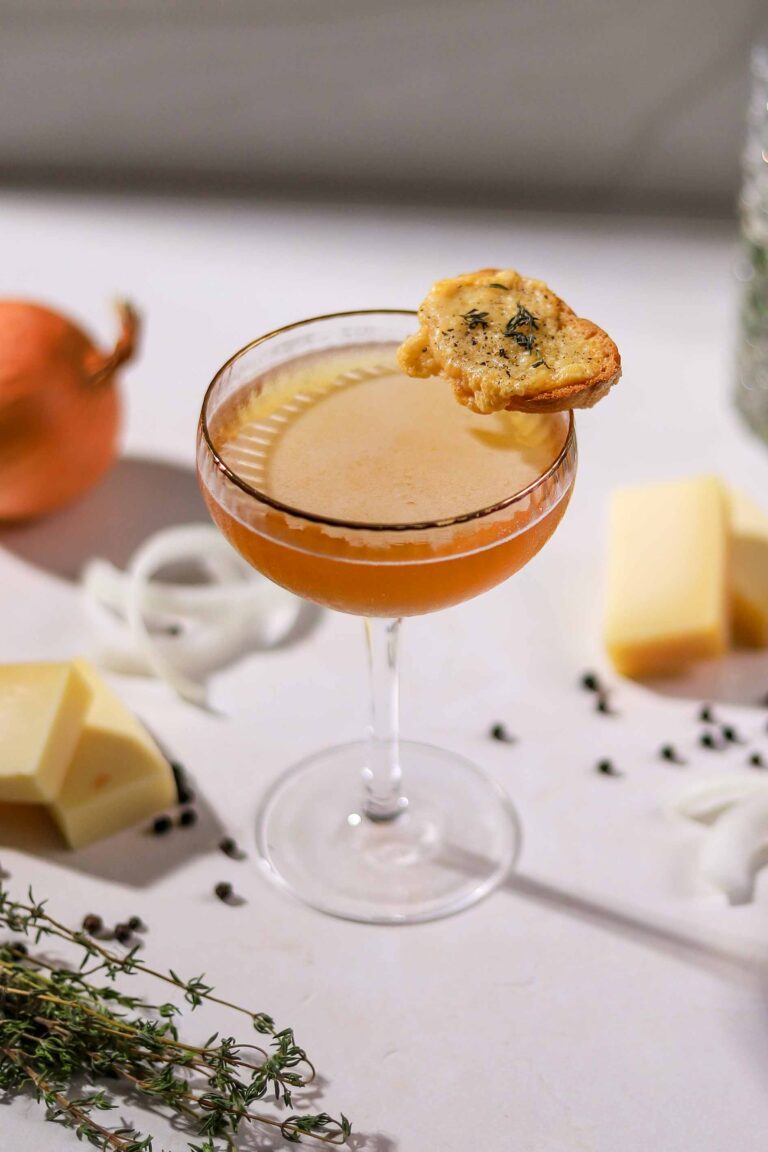 French onion soup martini in a coupe glass garnished with a Gruyère toast, with onions, thyme and cheese on the side