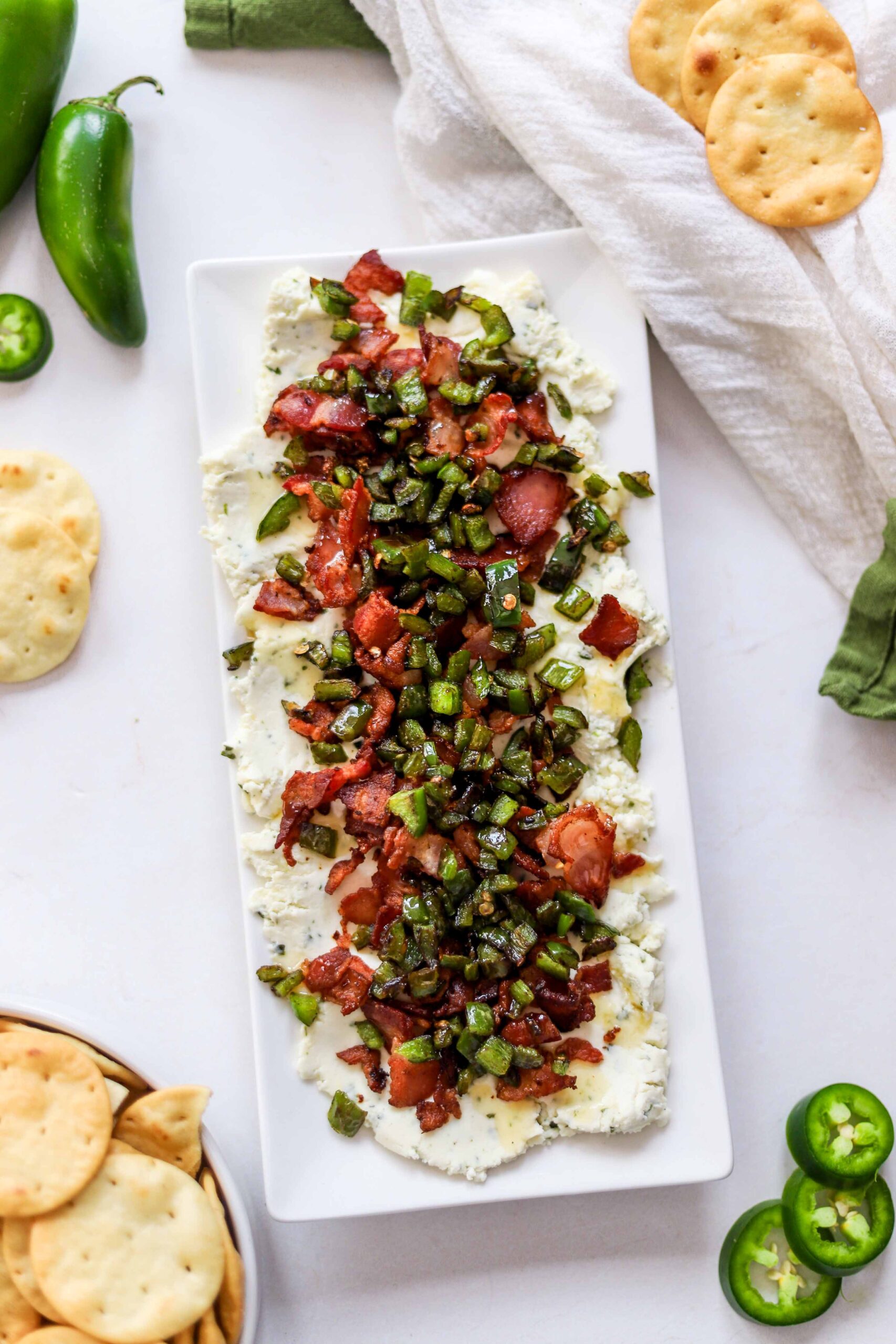 Boursin dip topped with crispy bacon, diced jalapeños and honey on a white serving plate