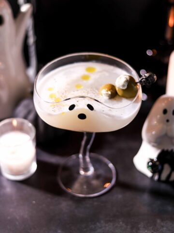 Burrata martini in a coupe glass with a ghost face, garnished with burrata-stuffed Castelvetrano olives on a pick