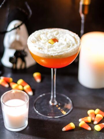 Candy corn martini in a coupe glass topped with whipped cream and candy corn