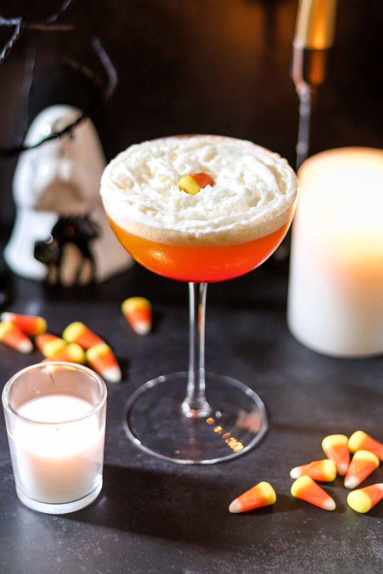 Candy corn martini in a coupe glass topped with whipped cream and candy corn
