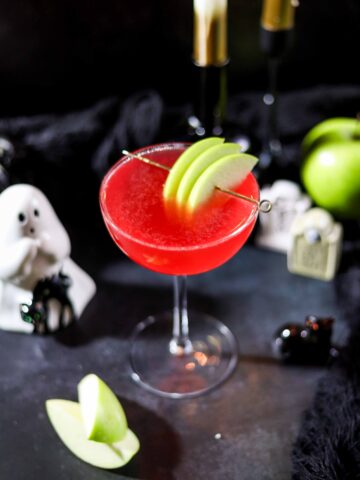 Bright red poison apple martini garnished with Granny Smith apple slices on a cocktail pick