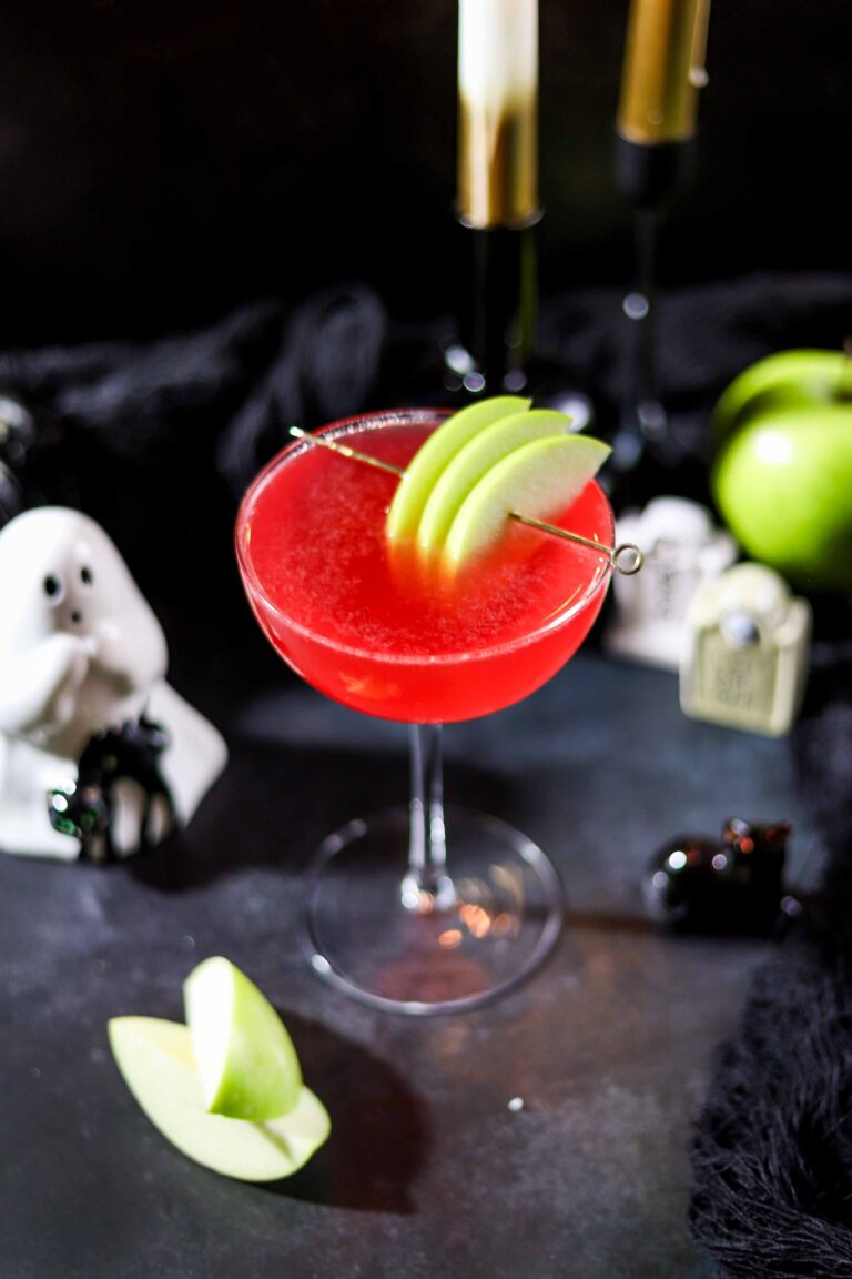 Bright red poison apple martini garnished with Granny Smith apple slices on a cocktail pick