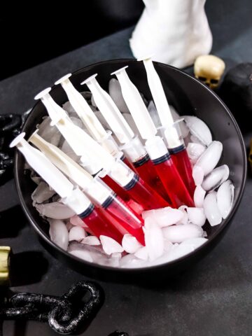Red syringe jello shots filled with cherry Jell-O and tequila, served on ice for Halloween